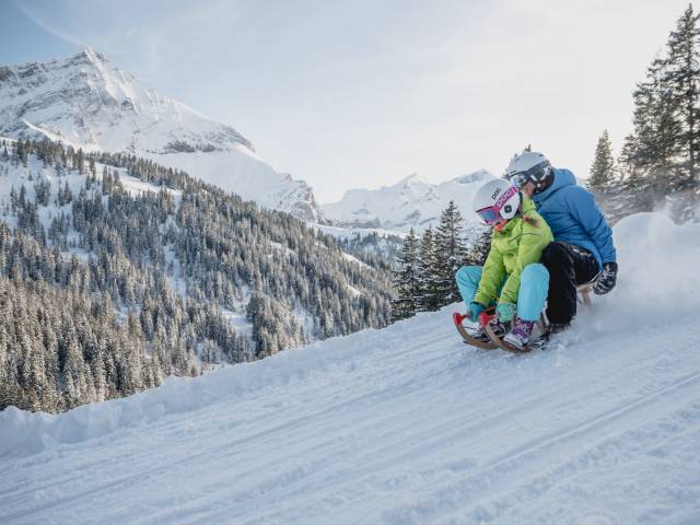 Vater und Kind beim Rodeln im Schnee in Gstaad in der Schweiz